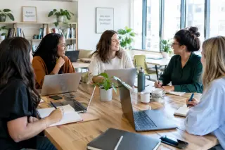 groupe de femmes entrepreneuses en réunion autour d'une table dans un espace de coworking lumineux, travaillant et discutant dans une ambiance conviviale