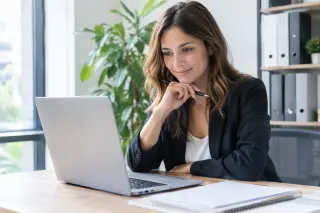 jeune femme seule au bureau travaillant sur son ordinateur portable, entourée de dossiers et de lumière naturelle